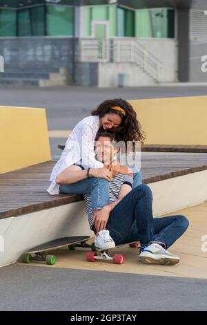 Un jeune couple amoureux s'assoit au coucher du soleil sur une longue planche. Homme et femme tendance qui se rafraîchvent en plein air Banque D'Images