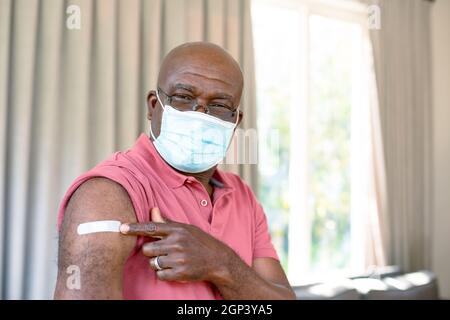 Homme afro-américain âgé sous masque montrant du plâtre après vaccination Banque D'Images