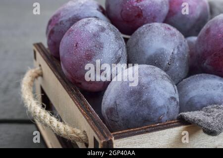 Sur la table dans un tiroir sont de grands prunes mûres. Présenté en gros plan sur un arrière-plan sombre. La vue du dessus. Banque D'Images