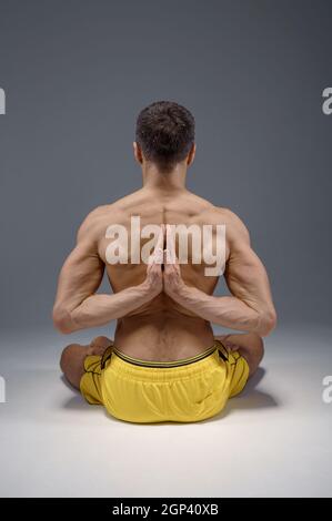 Le yoga est assis dans une posture classique avec les mains derrière son dos, position de méditation, étirement parfait, fond gris. Homme fort faisant de l'exercice yogi, haut Banque D'Images