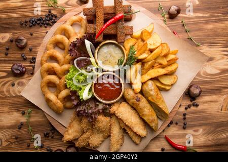 collation frite pour bière. Grande assiette d'en-cas de bière : croûtons, rondelles d'oignon frites en pâte, frites, quartiers de pommes de terre. Sauce chaude et sauce au fromage pour s Banque D'Images