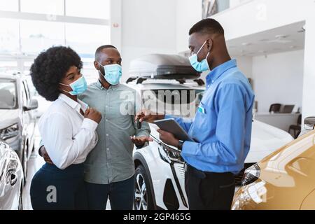 Couple noir dans le visage masques d'achat de nouvelle auto pendant le verrouillage covid, prenant la clé de voiture du vendeur à la concession automobile. Famille afro-américaine Banque D'Images