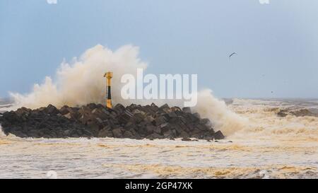 Une grande vague s'écrasant sur le brise-lames, le temps de tempête sur la côte atlantique à Anglet, en France. Mousse orange et ciel clair et nuageux avec tons bleus. Banque D'Images