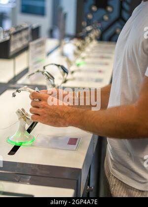 Vue latérale d'un client masculin méconnaissable se trouvant près de la vitrine et vérifiant la montre intelligente lors de ses achats dans un magasin d'électronique moderne Banque D'Images