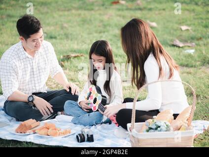 Joyeux père de famille asiatique jeune, mère et enfants s'amuser et profiter de l'extérieur ensemble assis sur la fête de l'herbe avec jouer Ukulele pendant un Banque D'Images