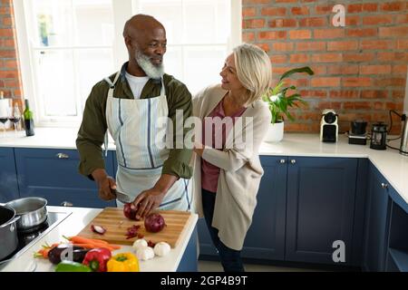 Heureux senior divers couple dans la cuisine de cuisiner ensemble, portant un tablier Banque D'Images