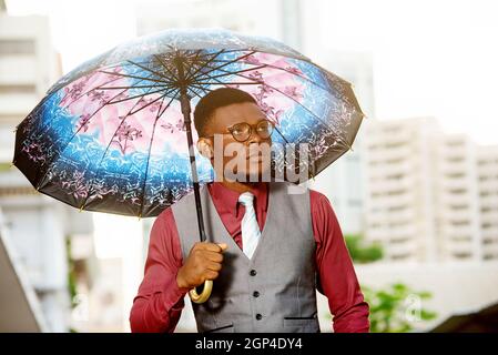 beau jeune homme attentionné, tenant un parapluie et regardant de côté sur l'extérieur Banque D'Images