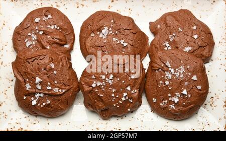Gros plan sur plusieurs biscuits ronds au chocolat au brownie fraîchement cuits avec du sel en flocons sur une assiette en porcelaine blanche, vue surélevée, directement au-dessus Banque D'Images