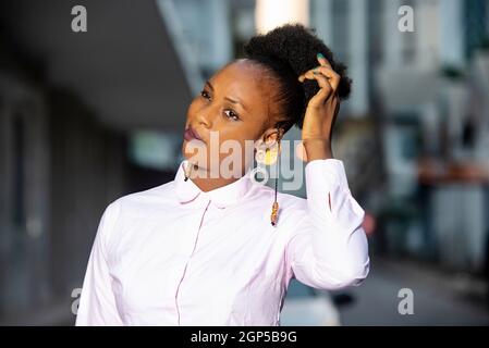 charmante jeune femme africaine debout à l'extérieur raclant ses cheveux. Banque D'Images
