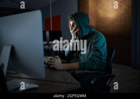 Un pirate Internet homme sérieux dans le capot fonctionne sur ordinateur, vue de face. Programmeur Web illégal sur le lieu de travail, profession criminelle. Piratage de données, cyber-secu Banque D'Images