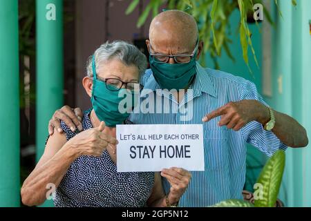 Un couple âgé, portant un masque et des lunettes et tenant un séjour à la maison chanter Banque D'Images