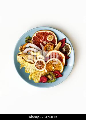 Croustilles de fruits séchées mélangées dans une plaque en céramique ronde sur fond blanc isolé. Vue de dessus, plan d'appartement Banque D'Images