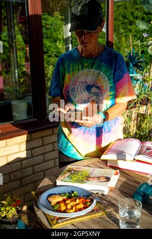 Une femme d'âge moyen prenant une photo d'une assiette de nourriture colorée. Il y a des livres de cuisine sur la table. Banque D'Images