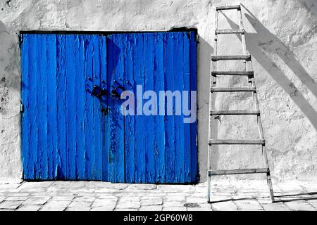Vue sur une porte en bois bleu avec poignées en métal et échelle penchée sur le mur à côté Banque D'Images