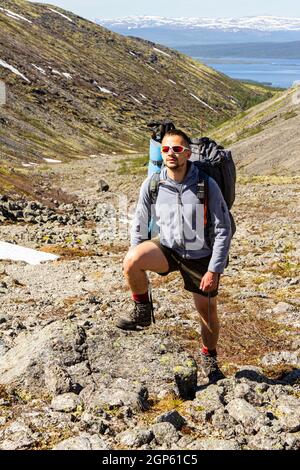 Un touriste européen en vêtements de sport avec de grands sacs à dos et des bâtons de randonnée monte sur une criée de pierre jusqu'au sommet des montagnes de Khibiny. Les randonneurs de groupe font Banque D'Images