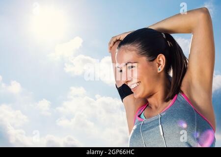 Gros plan d'un jeune coureur en train de se préparer pour la course du matin.Femme avec un sourire charmant qui s'étire les bras et le cou contre le ciel ensoleillé. Banque D'Images