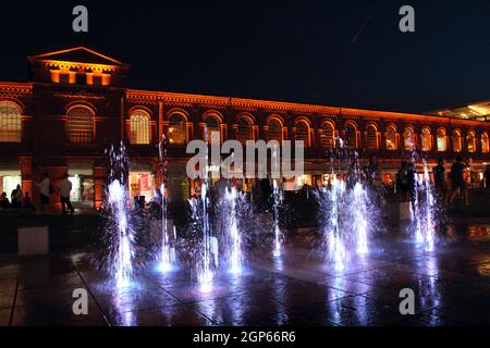 Les enfants jouent avec des fontaines de nuit dans la ville de Lodz. Magnifiques fontaines du soir. Les gens ont un repos près de beaux bâtiments éclairés la nuit. Banque D'Images