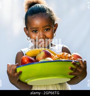 Portrait de la douce fille afro-américaine avec bol de fruits.isolé contre fond clair Banque D'Images