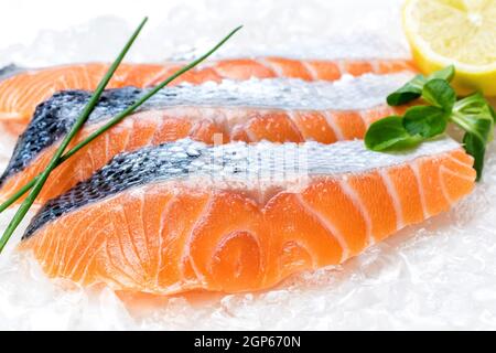 Gros plan macro de filets de saumon frais lacés sur de la glace pilée avec du citron et des verts en arrière-plan. Banque D'Images