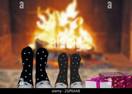 Un couple avec des chaussettes en laine de Noël et des boîtes-cadeaux assis détendu et confortable à l'intérieur près de la cheminée pendant une nuit d'hiver. Vacances d'hiver et de Noël an Banque D'Images