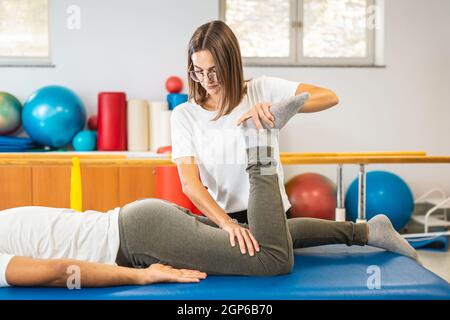 Physiothérapeute féminine effectuant des exercices d'étirement de la jambe avec un patient mâle en décubitus dorsal. Banque D'Images