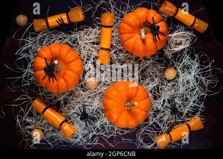 Citrouilles, bonbons, araignées et paille sur fond noir, concept de fête d'Halloween, vue du dessus Banque D'Images