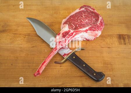 Steak Angus Tomahawk cru sur une planche de bois avec un couteau Banque D'Images