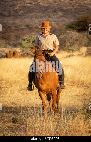 Blond souriant à cheval avec des buissons derrière Banque D'Images