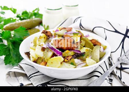 Salade de pommes de terre bouillies, bacon frit, oignons rouges et concombres marinés, assaisonnés de moutarde aux grains, d'épices et d'huile végétale dans une assiette sur une serviette Banque D'Images