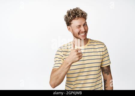 Beau blond homme se démène et sourit, montre les pouces dans l'approbation, louange travail parfait, bien fait geste, debout sur fond blanc Banque D'Images