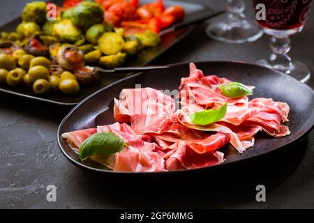 Prosciutto avec différents hors-d'œuvre avec un verre de vin rouge sur fond noir. Sur les légumes rôtis, en-cas sain Banque D'Images