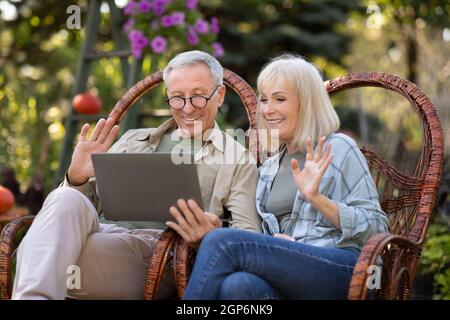Grands-parents modernes. Heureux conjoints âgés ayant des appels vidéo par ordinateur portable, se détendre dans des chaises en osier dans le jardin, communicationg avec la famille en ligne, copie s. Banque D'Images