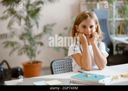 Une petite fille écrit dans un ordinateur portable pour faire ses devoirs au bureau dans une pièce lumineuse Banque D'Images