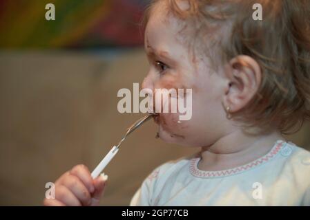 Petite fille mignonne mangeant son désert de chocolat après le dîner avec une cuillère et faire un sale visage sale Banque D'Images