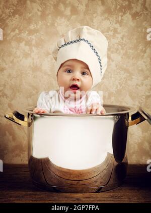 Mignon bébé chef dans un énorme chaudron sur table en bois Banque D'Images