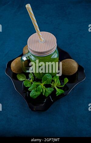 Smoothie aux feuilles de saladet au kiwi sur une assiette noire et décorée avec kiwi et laitue Banque D'Images