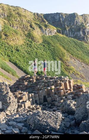 Jeune couple debout sur des colonnes de basalte, la chaussée des géants, Causeway Coast, près de Bushmills, comté d'Antrim, Irlande du Nord, Royaume-Uni Banque D'Images