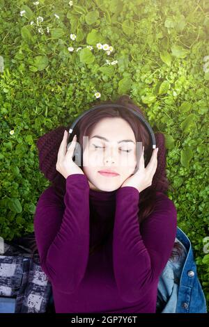 Belle jeune fille portant sur l'herbe en parc d'écouter de la musique avec des écouteurs. Vue de dessus et copyspace. Banque D'Images