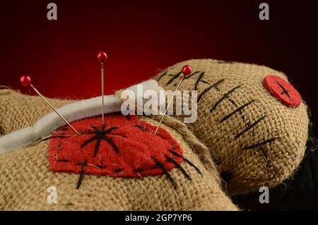 Quelques épingles sont collées à l'intérieur du coeur d'une poupée voodoo sur un fond rouge foncé et noir. Banque D'Images