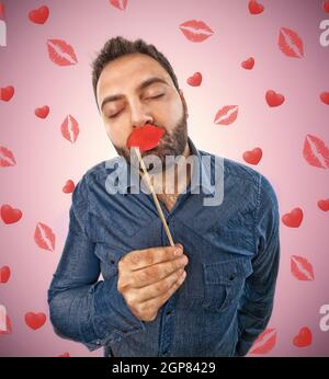 Jeune homme avec Photo Booth et l'arrière-plan en forme de lèvres de baisers et les cœurs Banque D'Images