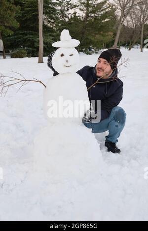 Jeune homme caucasien faisant un smiley bonhomme de neige avec un chapeau Banque D'Images