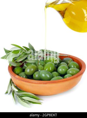 L'huile d'olive découlant d'une cruche en terre cuite dans un bol avec les branches d'un olivier Banque D'Images