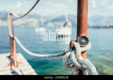 Boussole sur un couché sur une corde à l'océan, bateaux à voile et à l'arrière-plan flou Banque D'Images