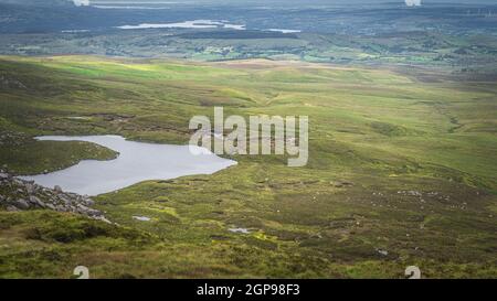 Vue depuis la montagne Cuilcagh sur les lacs, les prairies verdoyantes et les champs avec des taches de lumière du soleil dans la vallée ci-dessous, Irlande du Nord Banque D'Images