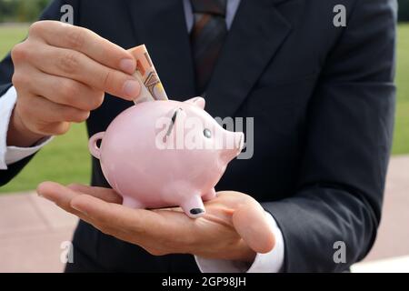 L'homme d'affaires nourrit la banque de porc avec le billet de banque allemand - concept d'économie fonds de prêt investissant de l'argent Banque D'Images