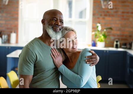 Joyeux couple senior varié dans la cuisine accueillant et souriant Banque D'Images