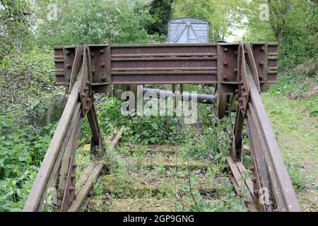 Heritage ligne de chemin de fer magasin extérieur avec des tampons, roues de bogie avec et sans chariot de marchandises sur la courte section de voie avec de grands arbres. Banque D'Images