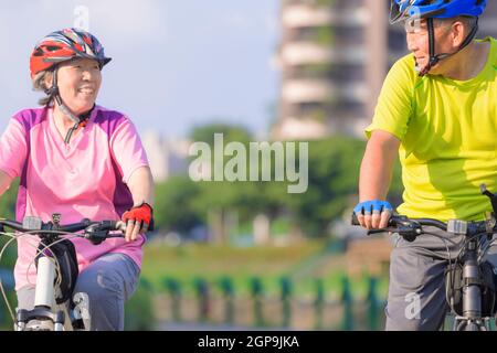 Joyeux couple asiatique senior s'entraîner avec des vélos dans le parc de la ville Banque D'Images