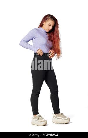 Une jeune femme de race blanche touche sa ceinture avec des cheveux longs et des vêtements décontractés. Banque D'Images