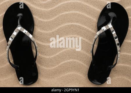 Paire de sandales de plage noire en strass, cette position sur le sable. Vue de dessus Banque D'Images